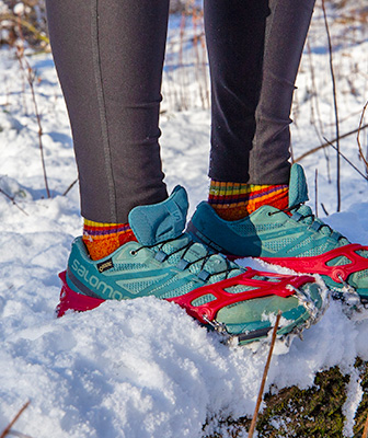 Trail running shoes in the snow with traction device.