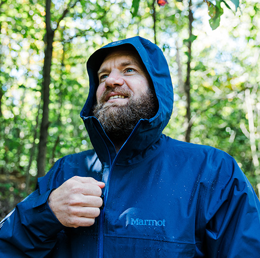 man outdoors putting on rain jacket